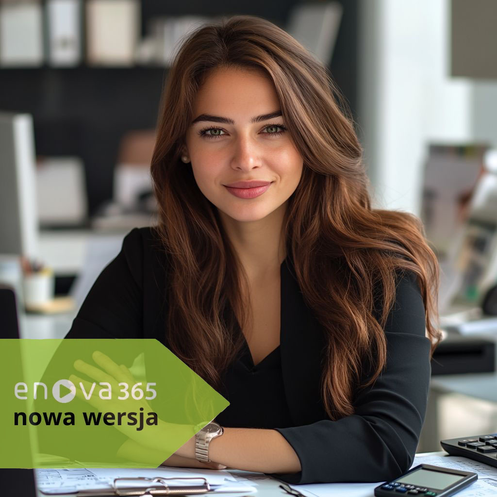 kobieta szatynka o długich włosach, księgowa siedząca przy swoim biurku wśród dokumentów, monitora, klawiatury i patrząca wprost